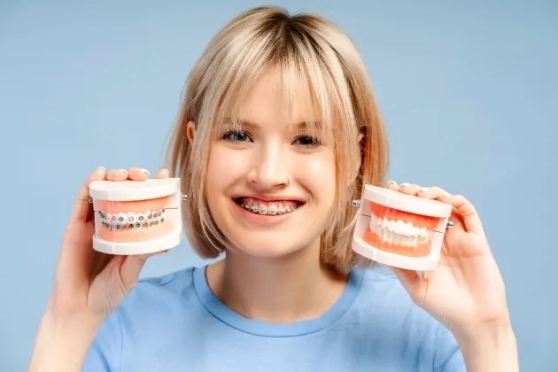 Pacient cu aparat dentar cu bracketi tinand in mana si aparat dentar transparent