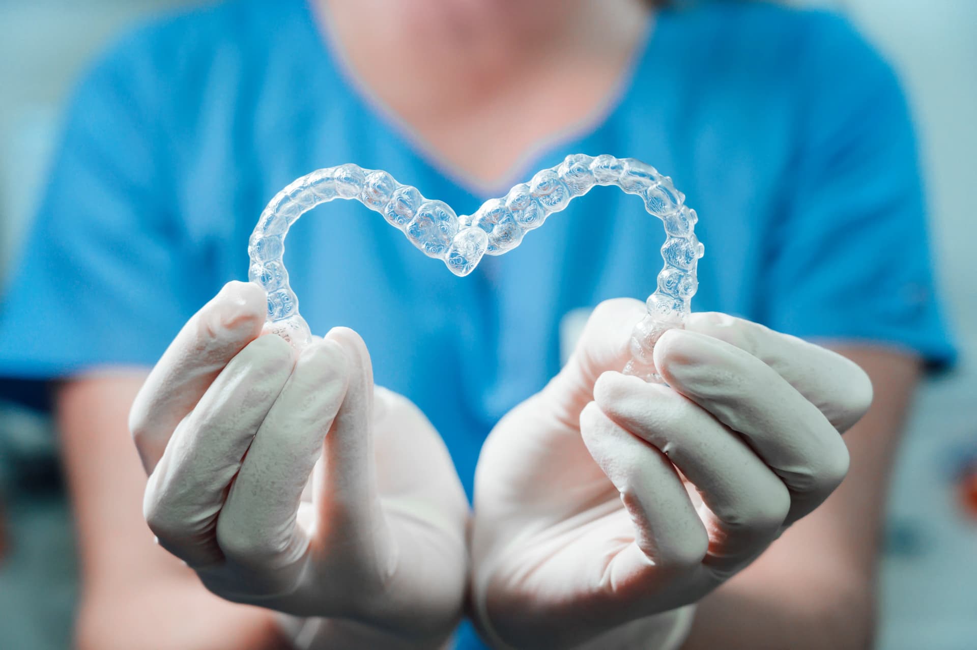 Dental professional holding transparent clear aligner shaped like a heart.