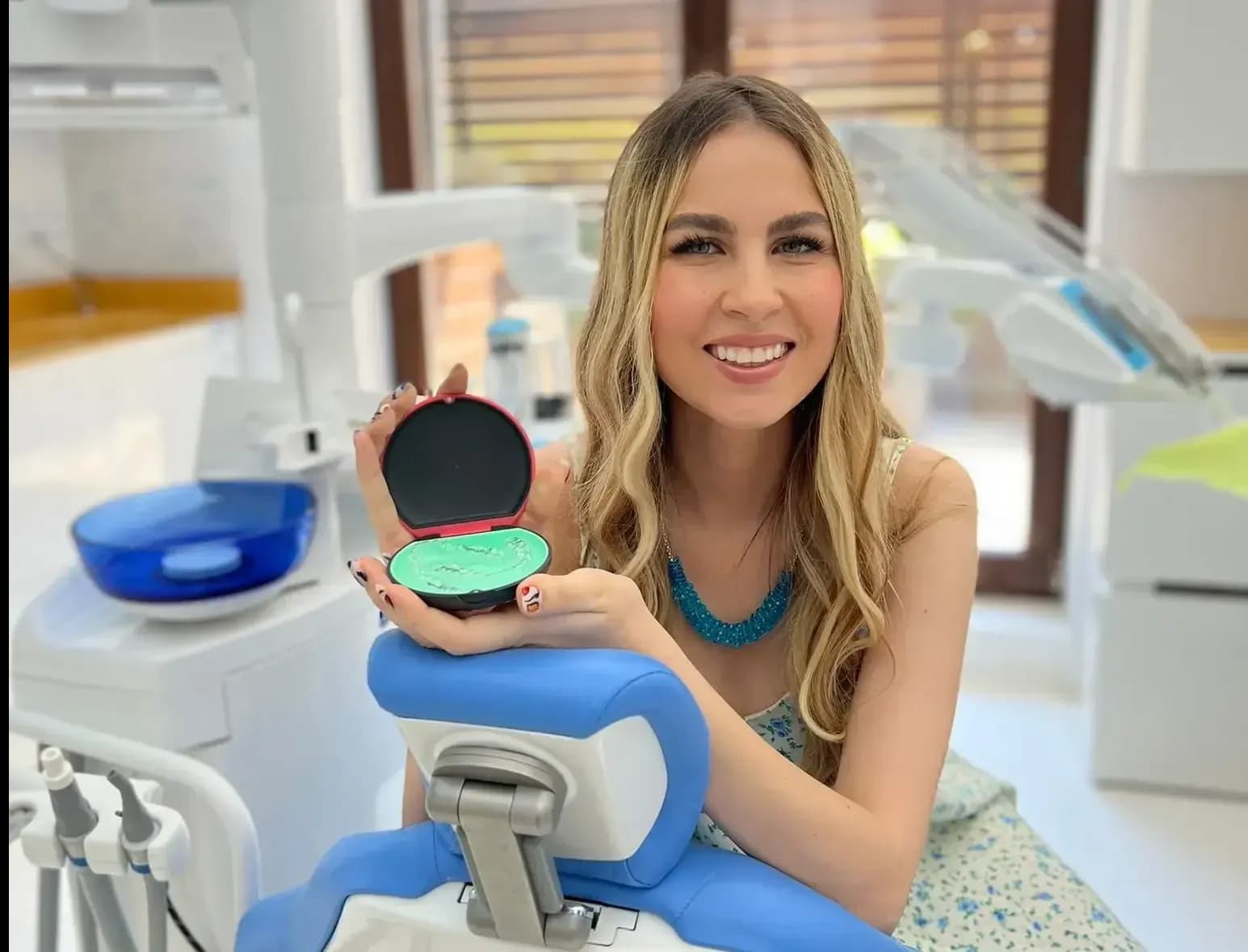 Patient smiling on dental chair holding clear aligner case