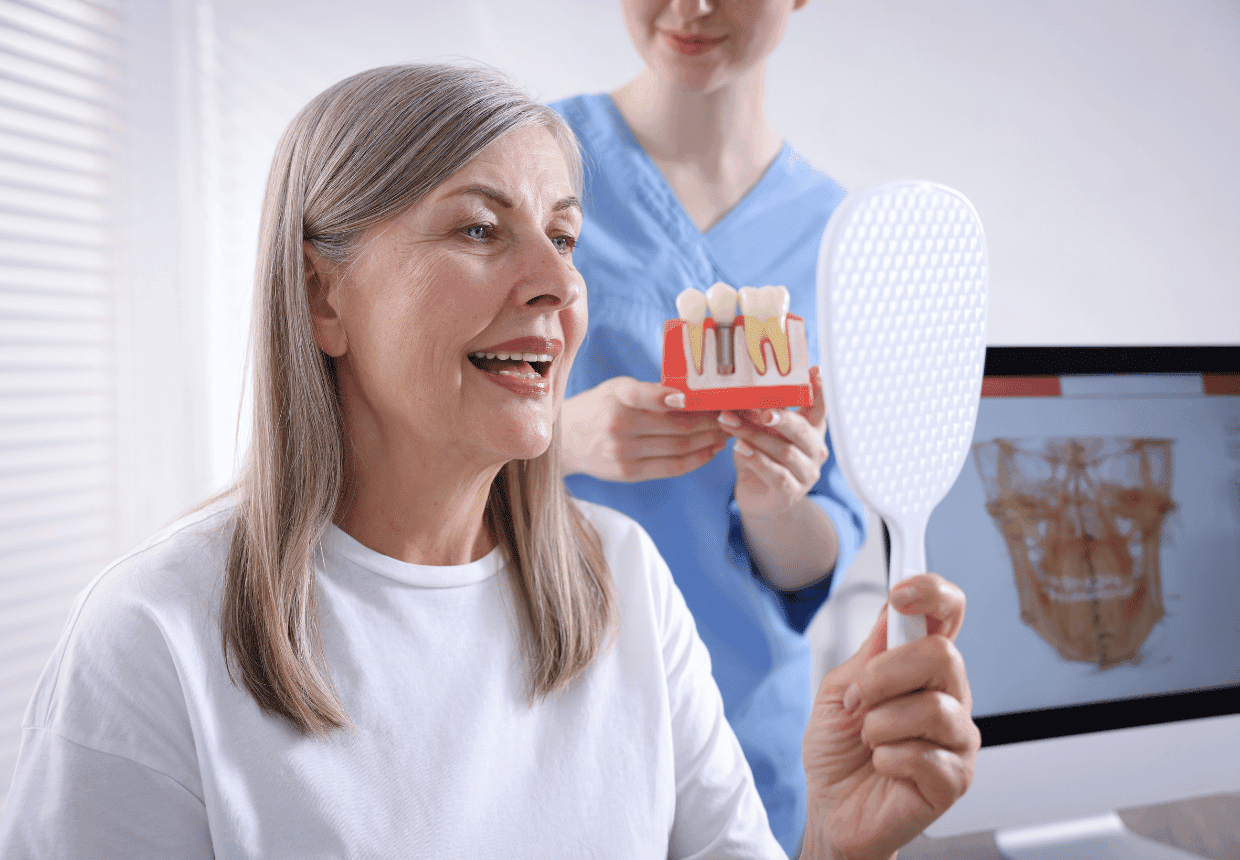 Pacientă privește în oglindă la zâmbetul refăcut cu implant dentar în zonă frontală