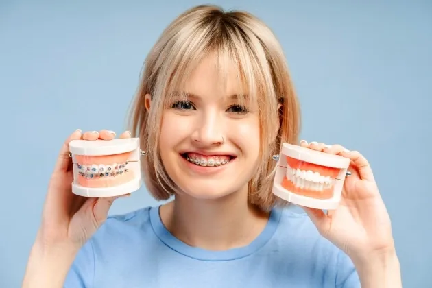 Pacient cu aparat dentar cu bracketi tinand in mana si aparat dentar transparent